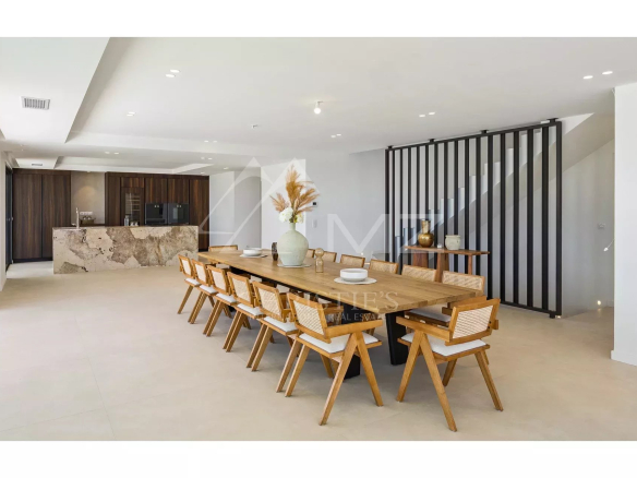 Intérieur d'une villa contemporaine avec une grande table à manger en bois et un coin cuisine.