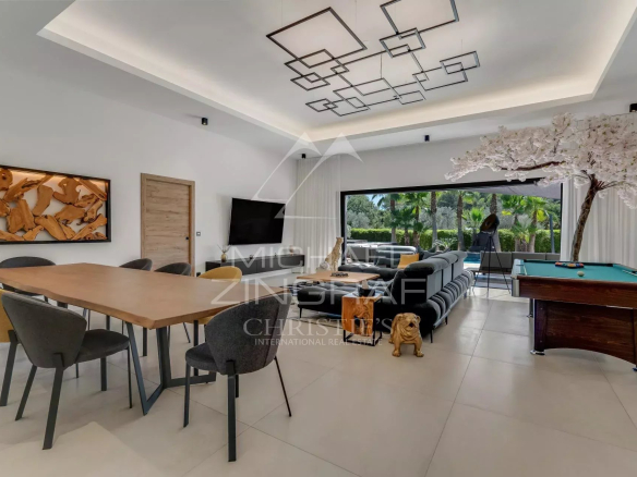 Intérieur d'une villa contemporaine avec salle à manger et salon, piscine visible à l'extérieur.