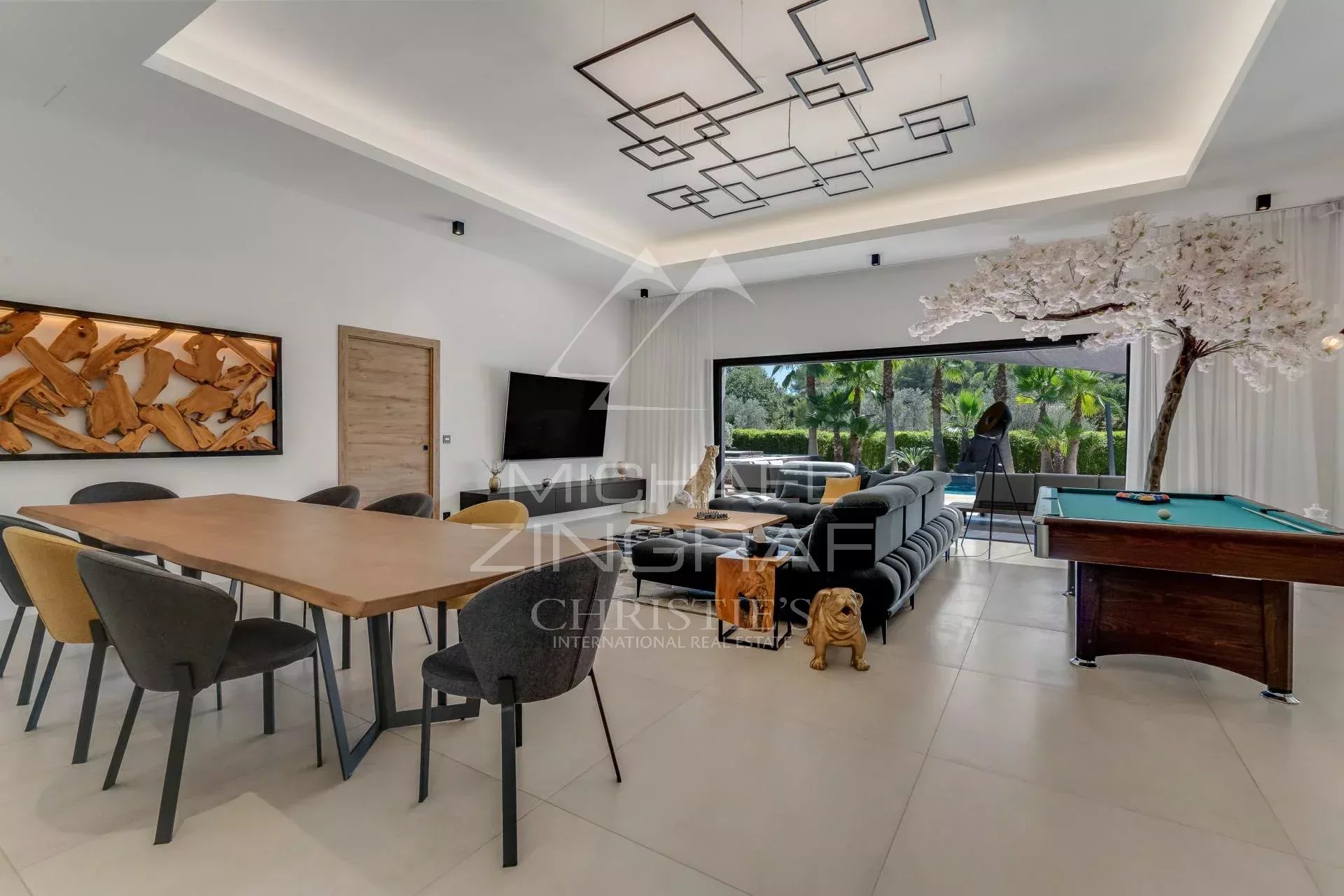 Intérieur d'une villa contemporaine avec salle à manger et salon, piscine visible à l'extérieur.