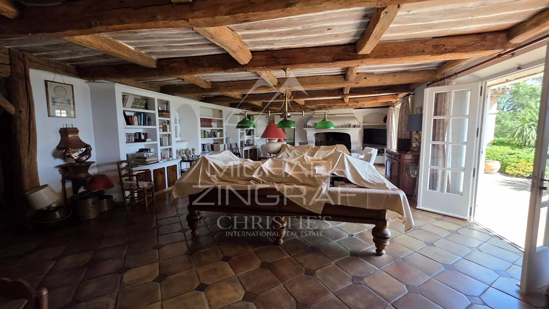 Intérieur d'une villa avec poutres en bois et mobilier traditionnel, vue sur un jardin.