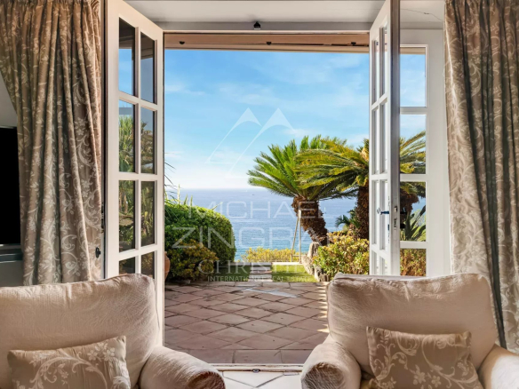 Vue depuis une villa avec des fauteuils, ouvrant sur un jardin et la mer.
