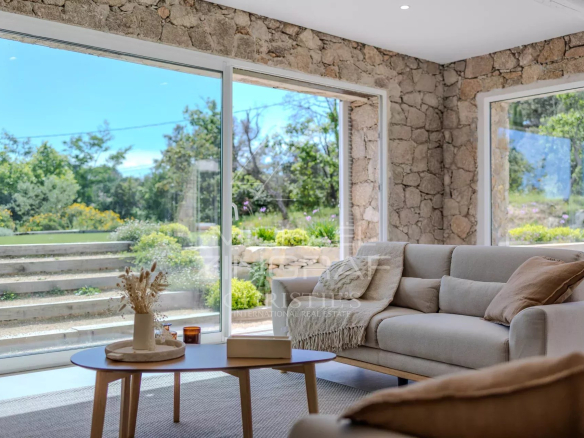 Intérieur d'une villa en pierre rénovée avec un salon lumineux et des fenêtres donnant sur le jardin.