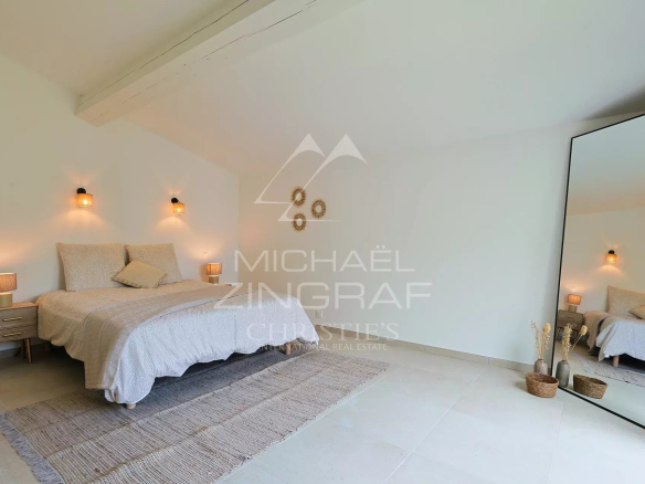 Chambre spacieuse d'une villa en pierre rénovée avec lit et miroir, décor minimaliste.