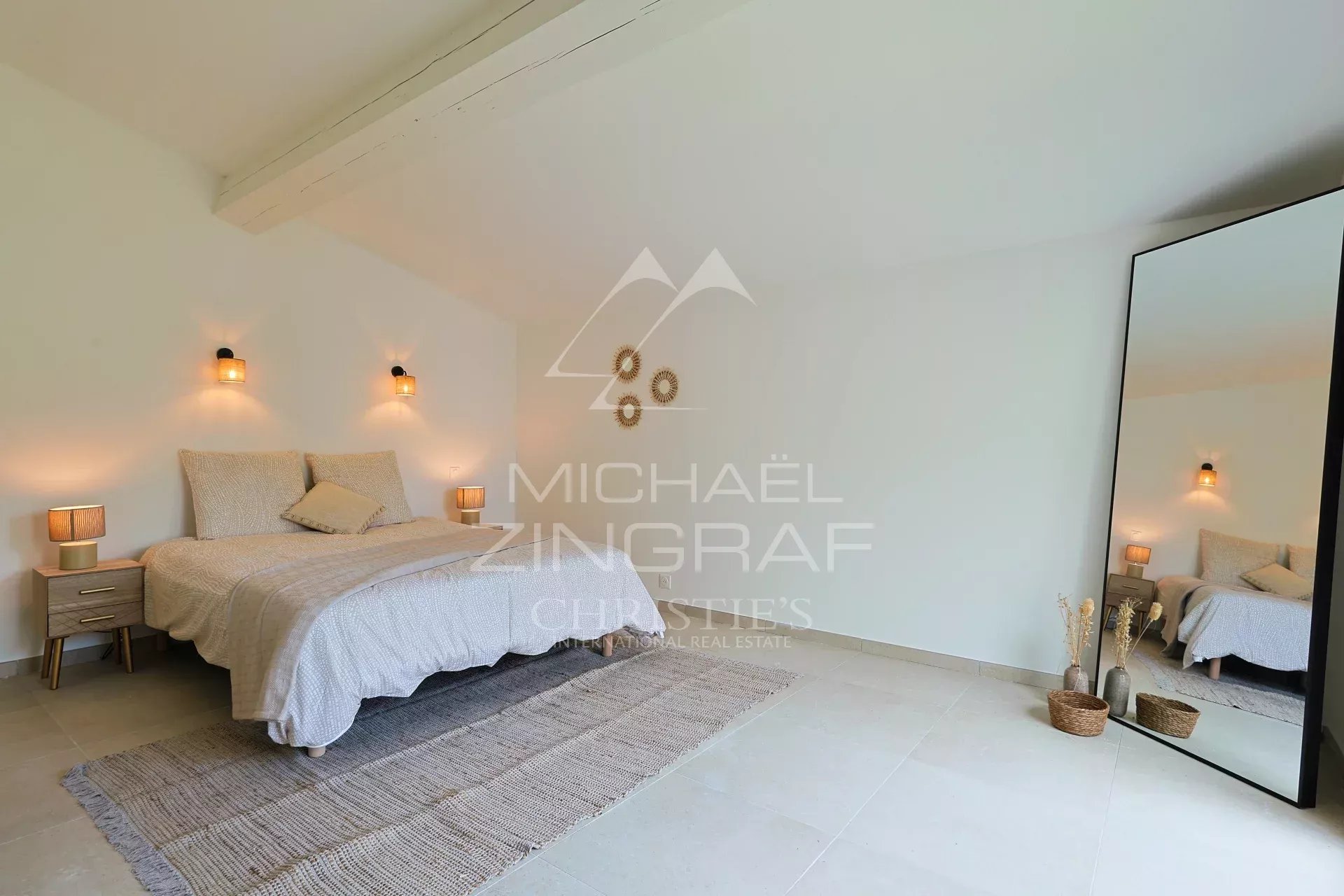 Chambre de villa rénovée Chambre spacieuse d'une villa en pierre rénovée avec lit et miroir, décor minimaliste.