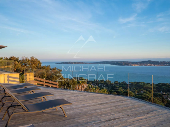 Panoramic view of the Gulf of Saint-Tropez from a wooden terrace with sun loungers.