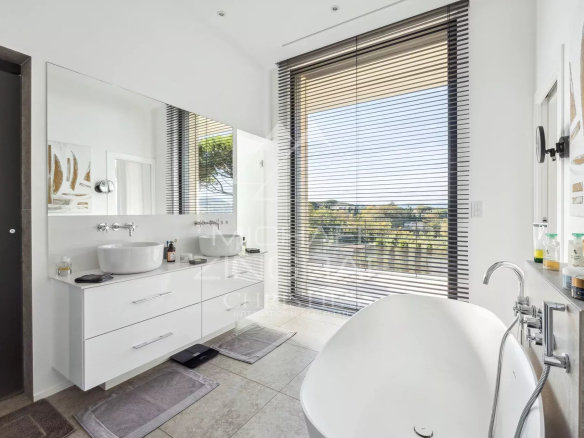 Salle de bain moderne avec baignoire, miroir et vue sur la nature à Saint-Tropez.