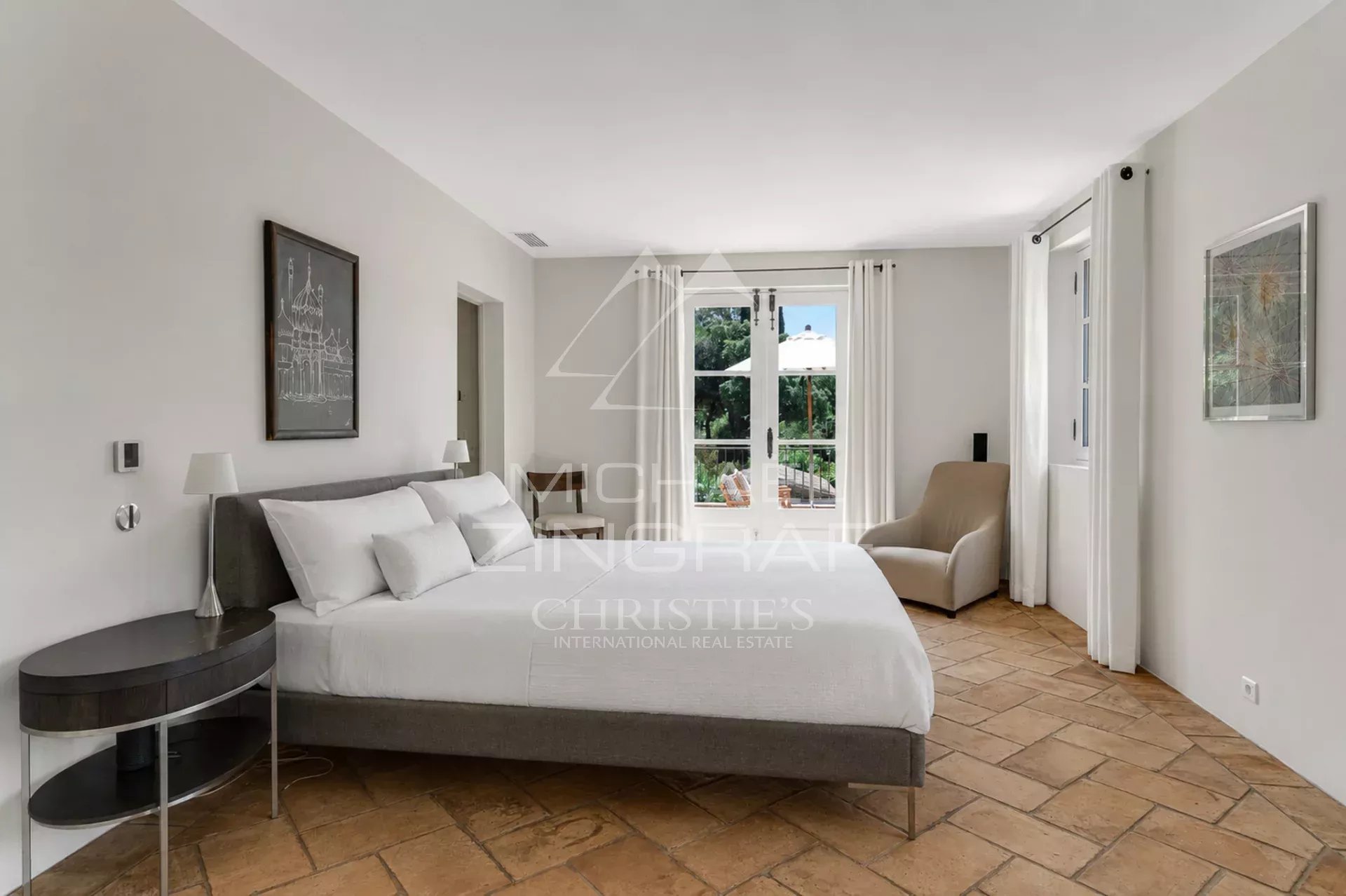 Chambre d'une villa provençale à Ramatuelle avec lit double et fenêtres donnant sur le jardin.