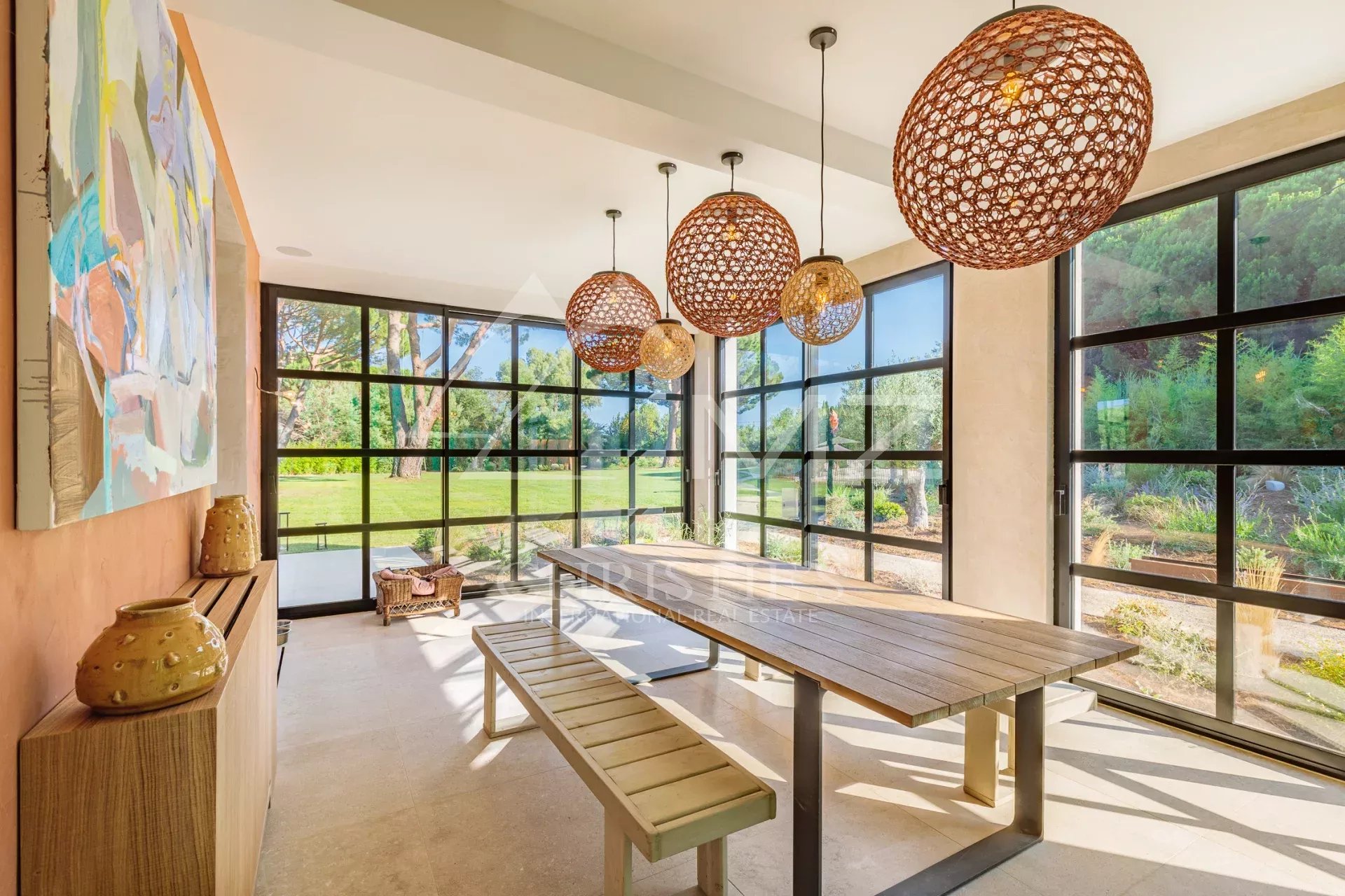 Salle à manger lumineuse de la Villa Shesh Salle à manger en véranda avec grandes fenêtres et mobilier en bois, vue sur le jardin.