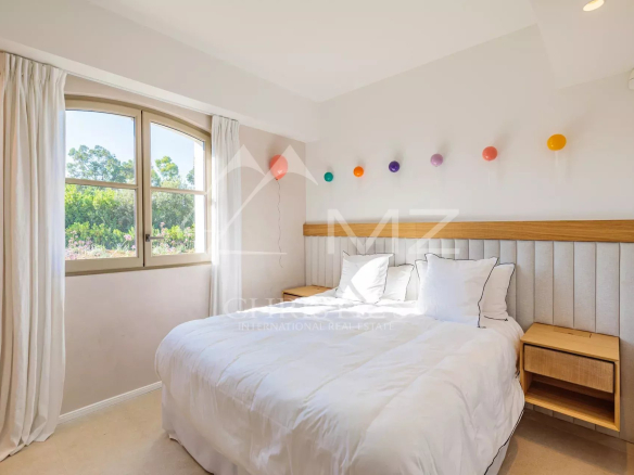 Chambre d'une villa neuve à Ramatuelle avec lit double et fenêtre donnant sur un parc.