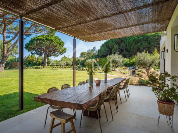 Terrasse d'une villa avec une grande table en bois, entourée d'un parc paysager.