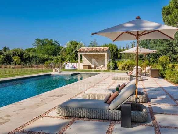 Piscine avec chaises longues et parasols dans un parc paysager.