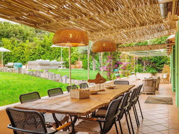 Terrasse ensoleillée d'une villa avec table en bois et chaises, entourée de verdure à Gassin.