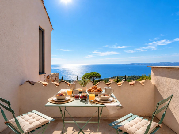 Terrasse avec vue sur la mer, table dressée avec petits-déjeuners, ciel bleu et mer en arrière-plan.