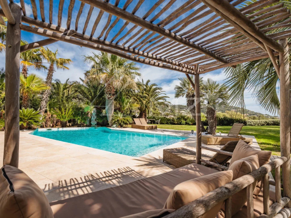 Terrasse en bois avec vue sur la piscine entourée de palmiers dans une villa à Grimaud.