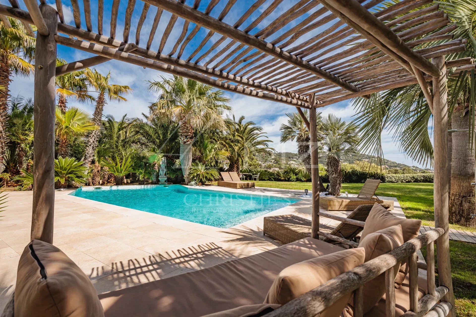 Villa de standing avec piscine à Grimaud Terrasse en bois avec vue sur la piscine entourée de palmiers dans une villa à Grimaud.