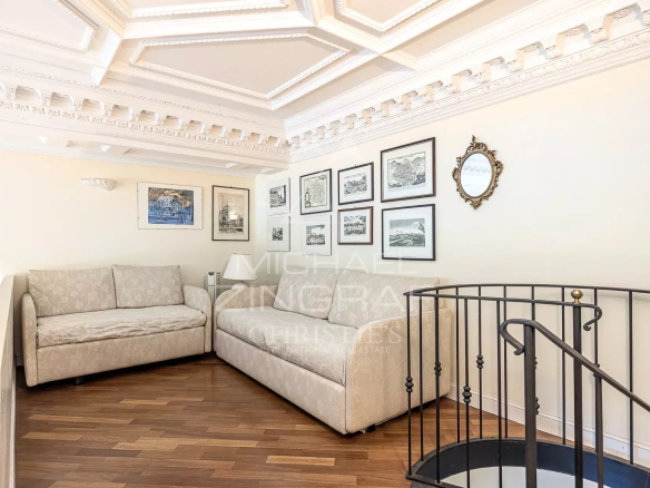 Cozy living corner with two beige patterned sofas, white ornate ceiling, and a wall of framed black-and-white art.