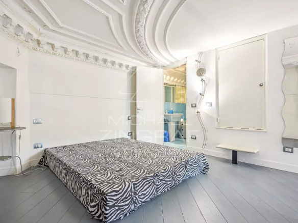 Bedroom with a zebra-patterned bedspread, ornate white ceiling molding, and an open door to a blue-tiled bathroom at the side.