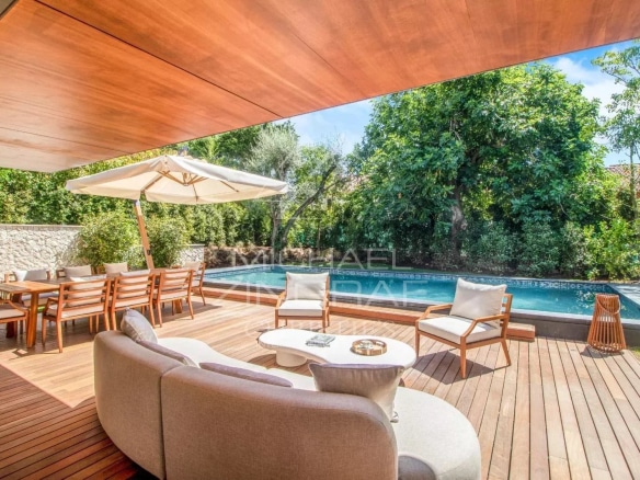 Terrace of a contemporary villa with swimming pool in Saint-Jean-Cap-Ferrat, wooden furniture and parasol.
