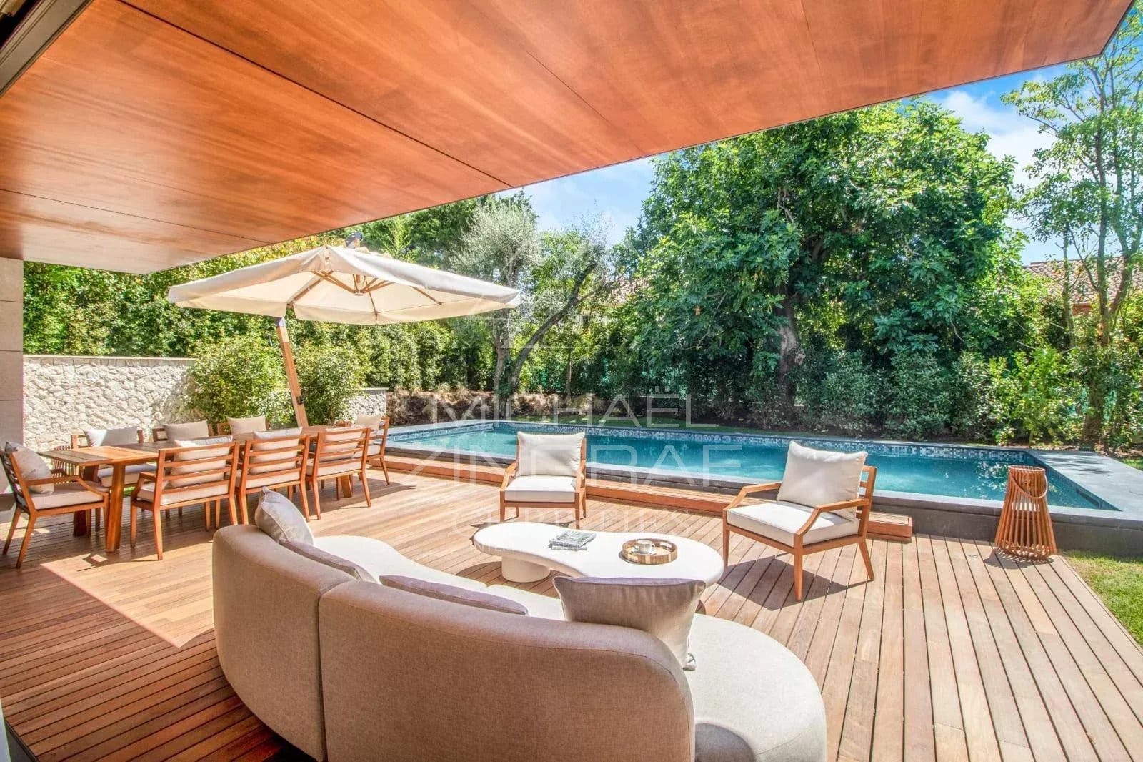 Terrace of a contemporary villa with swimming pool in Saint-Jean-Cap-Ferrat, wooden furniture and parasol.