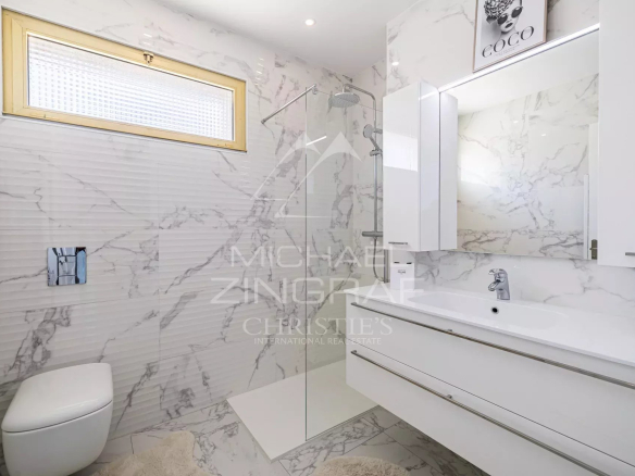 Salle de bain moderne avec carrelage en marbre et mobilier blanc.