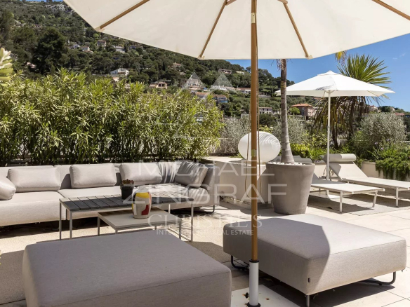Terrasse d'un appartement à Èze avec mobilier moderne et parasol, vue sur la verdure environnante.