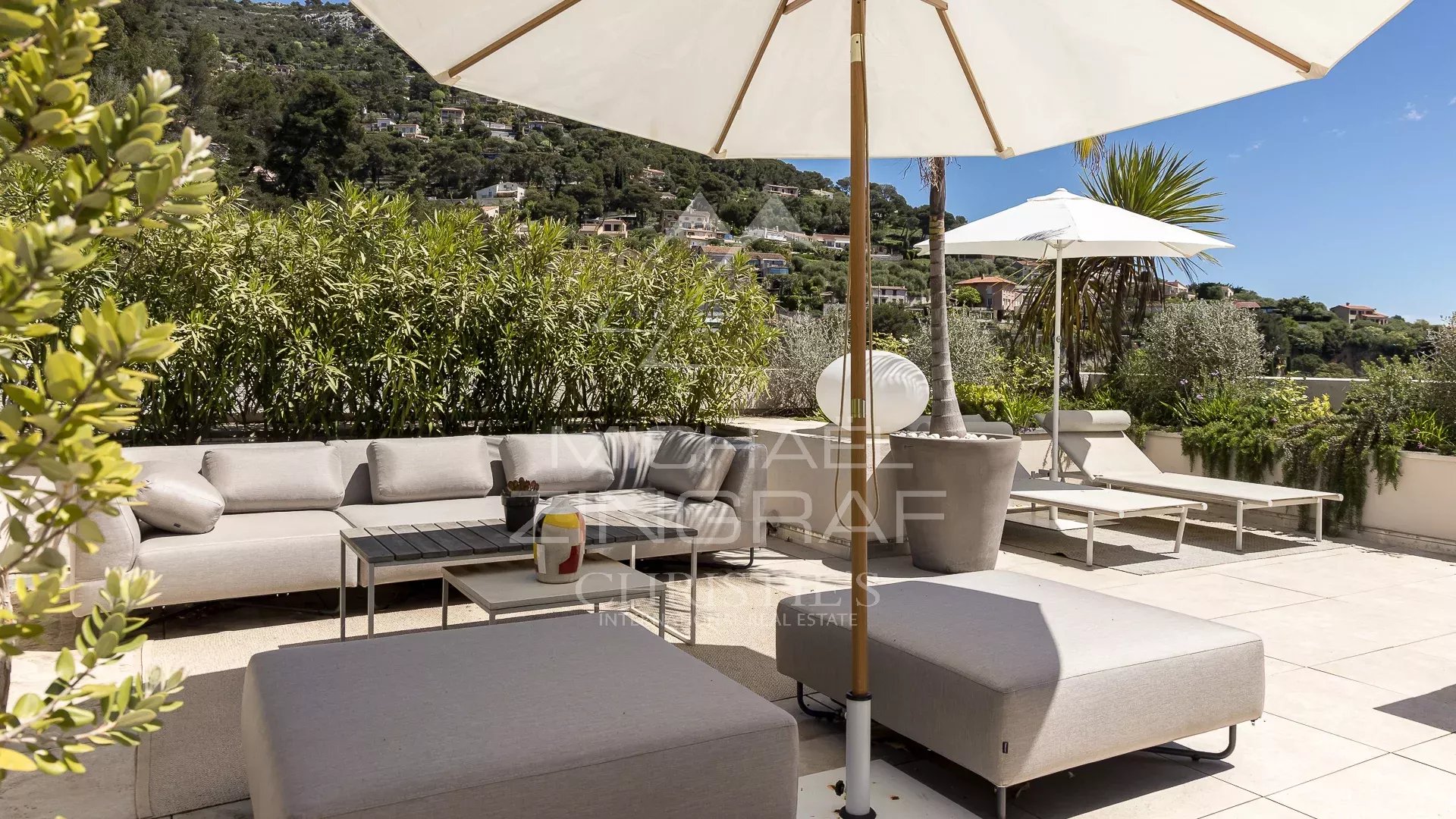 Terrasse d’un appartement à Èze Terrasse d'un appartement à Èze avec mobilier moderne et parasol, vue sur la verdure environnante.