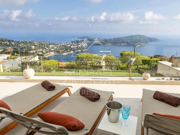 Vue panoramique sur la rade de Villefranche-sur-Mer depuis une terrasse avec transats.