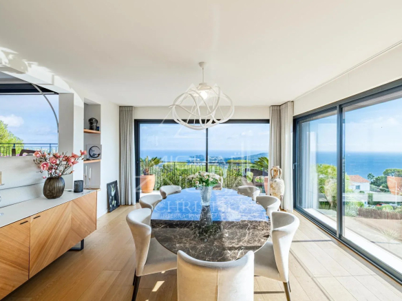 Intérieur d'une villa contemporaine avec vue sur la mer, table à manger et grandes baies vitrées.