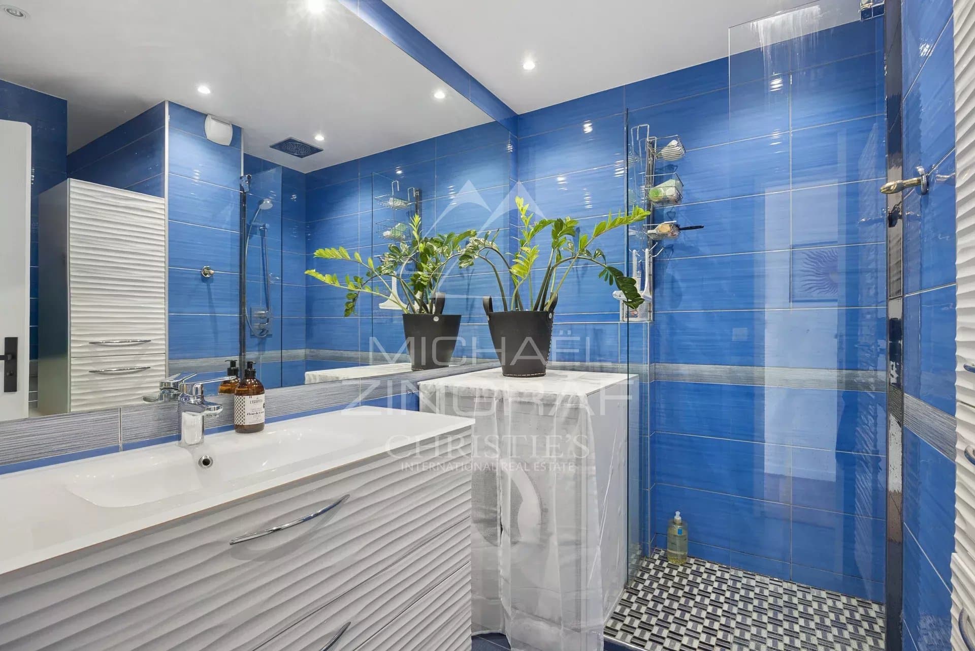 Elegant bathroom in Cap d'Antibes Modern bathroom with blue tiles and potted plants.