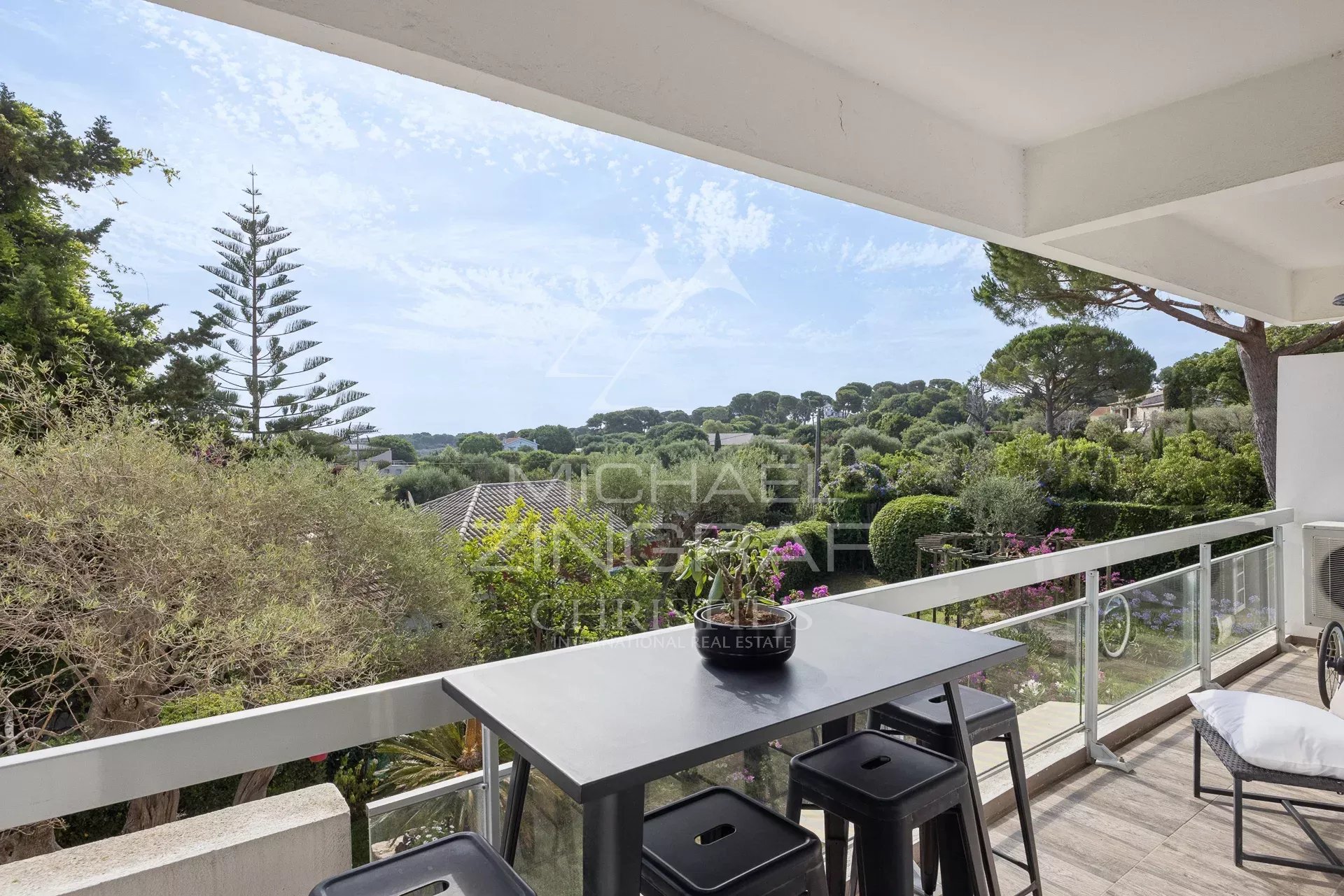 Balcony with a view at Cap d'Antibes View from a balcony of an apartment with a table and chairs, surrounded by greenery in Cap d'Antibes.