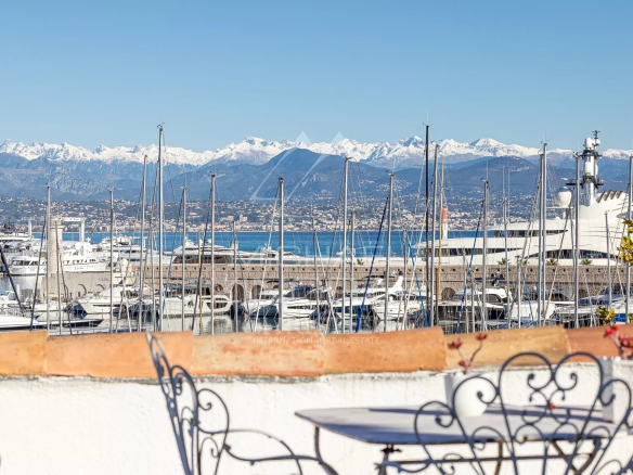 Vue panoramique sur le port d'Antibes avec des voiliers et les montagnes en arrière-plan.
