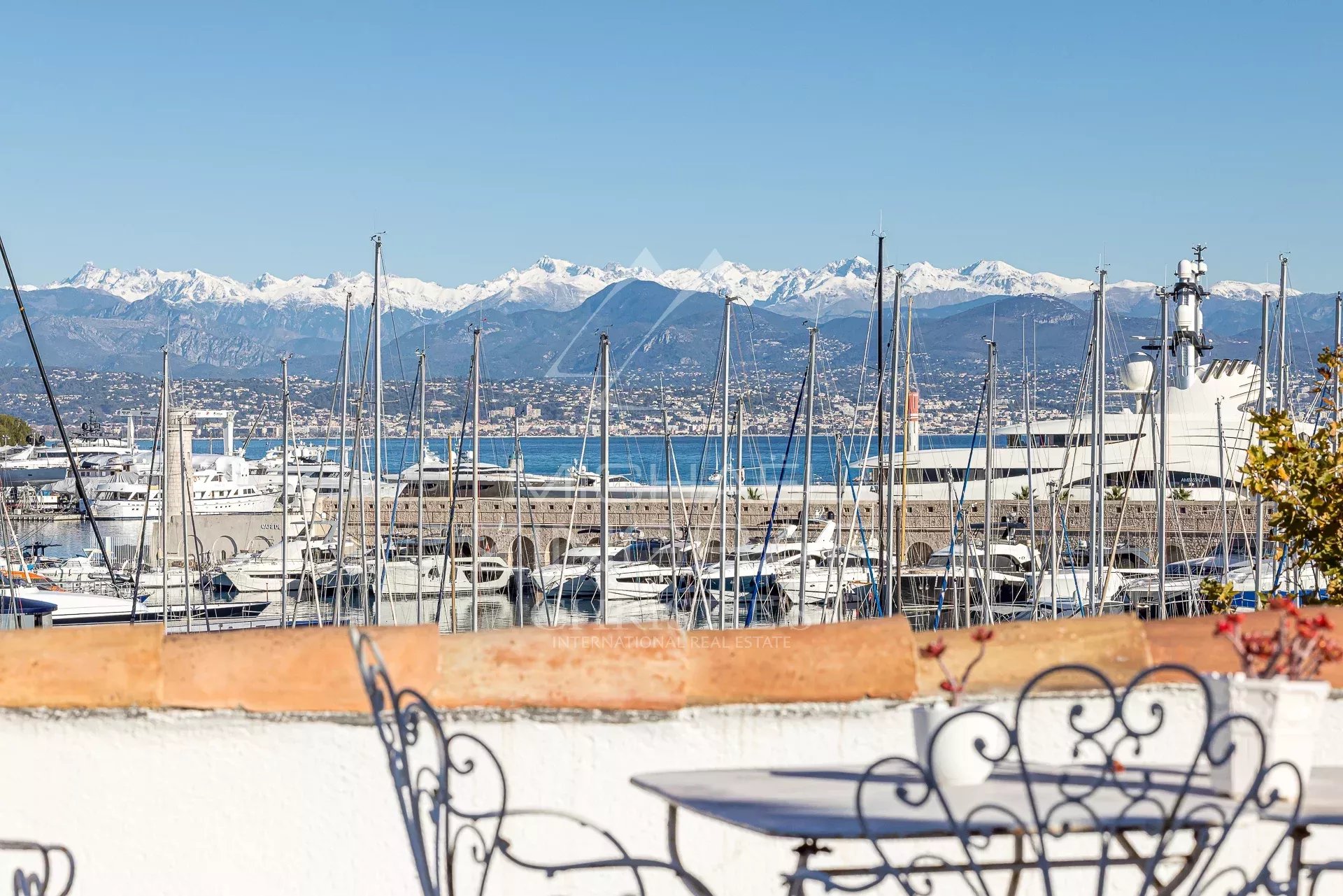 Vue panoramique sur le port d'Antibes avec des voiliers et les montagnes en arrière-plan.