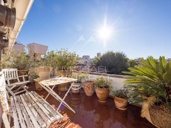 Terrasse ensoleillée avec plantes et mobilier, vue sur la ville d'Antibes.