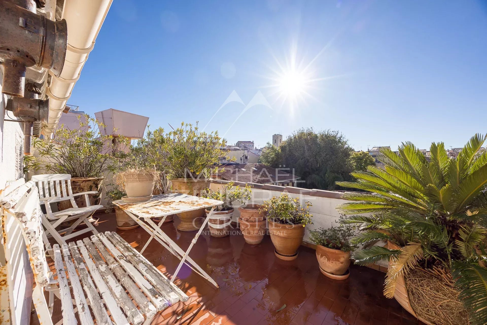 Terrasse ensoleillée avec plantes et mobilier, vue sur la ville d'Antibes.