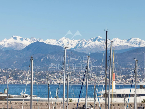 Vue panoramique des montagnes et du port d'Antibes avec des voiliers au premier plan.