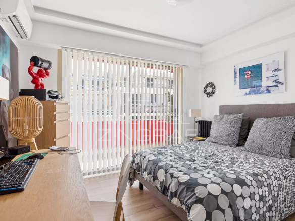 Chambre d'un appartement rénové avec lit double et bureau, fenêtres avec stores à lamelles.
