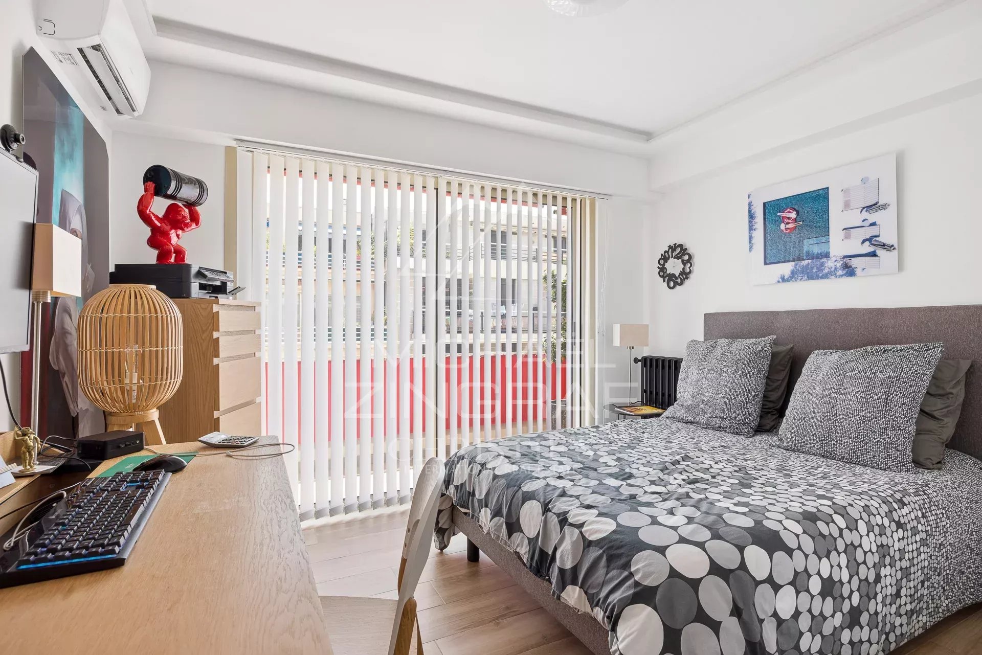 Chambre d'un appartement rénové avec lit double et bureau, fenêtres avec stores à lamelles.