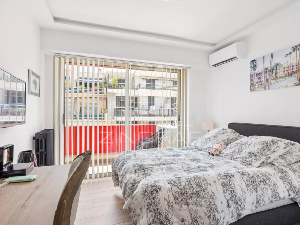 Chambre d'un appartement rénové avec lit double et télévision, vue sur un balcon.
