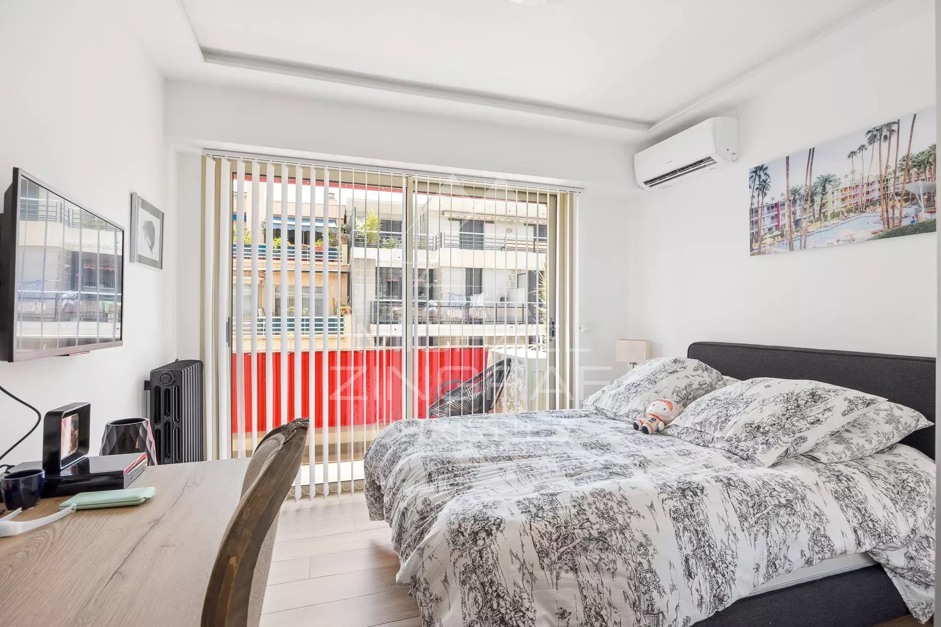 Chambre d'un appartement rénové avec lit double et télévision, vue sur un balcon.