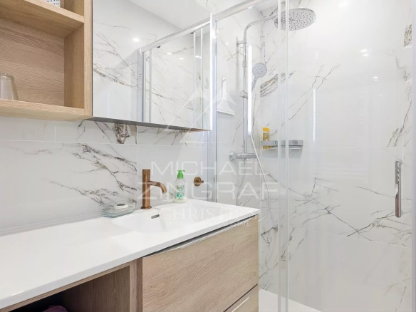Salle de bain moderne avec douche en verre et meuble en bois clair.