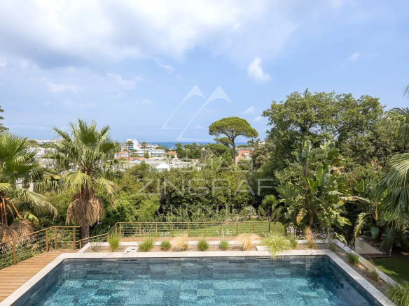 View of the pool and garden of a contemporary villa in Antibes, with palm trees and a view of the sea.