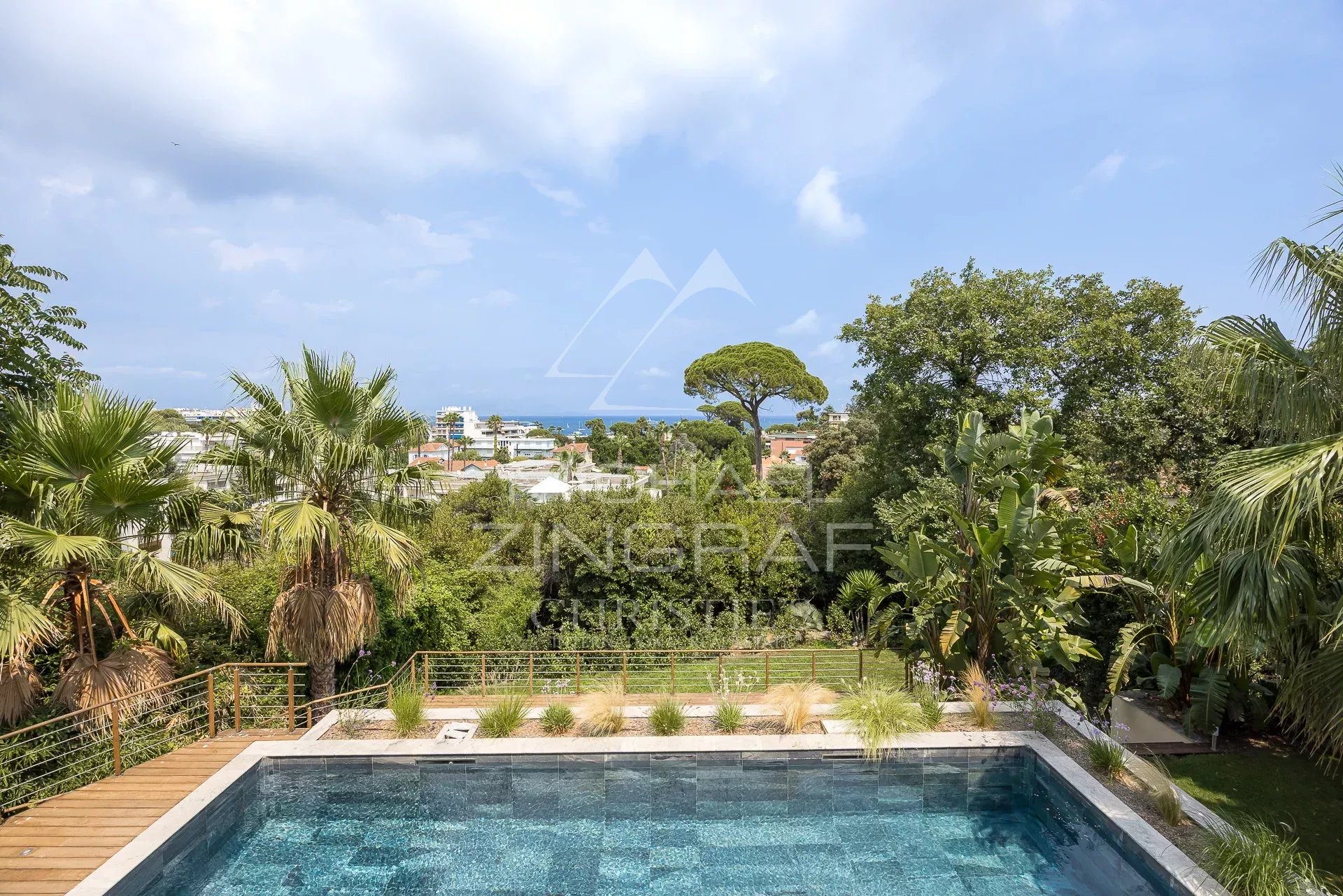 View of the pool and garden of a contemporary villa in Antibes, with palm trees and a view of the sea.