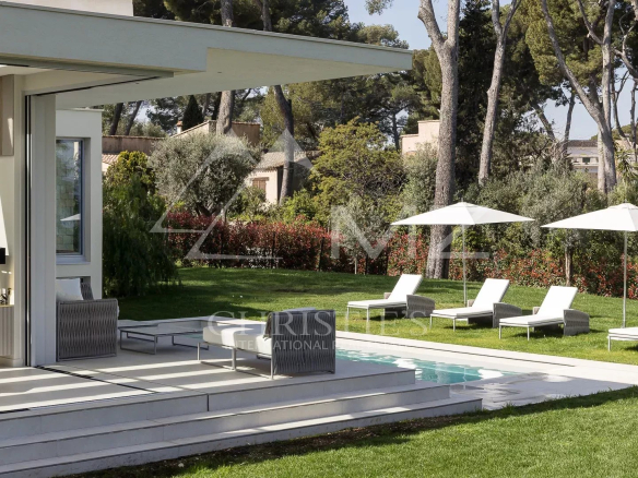 Villa moderne avec piscine et chaises longues dans un jardin verdoyant à Antibes.