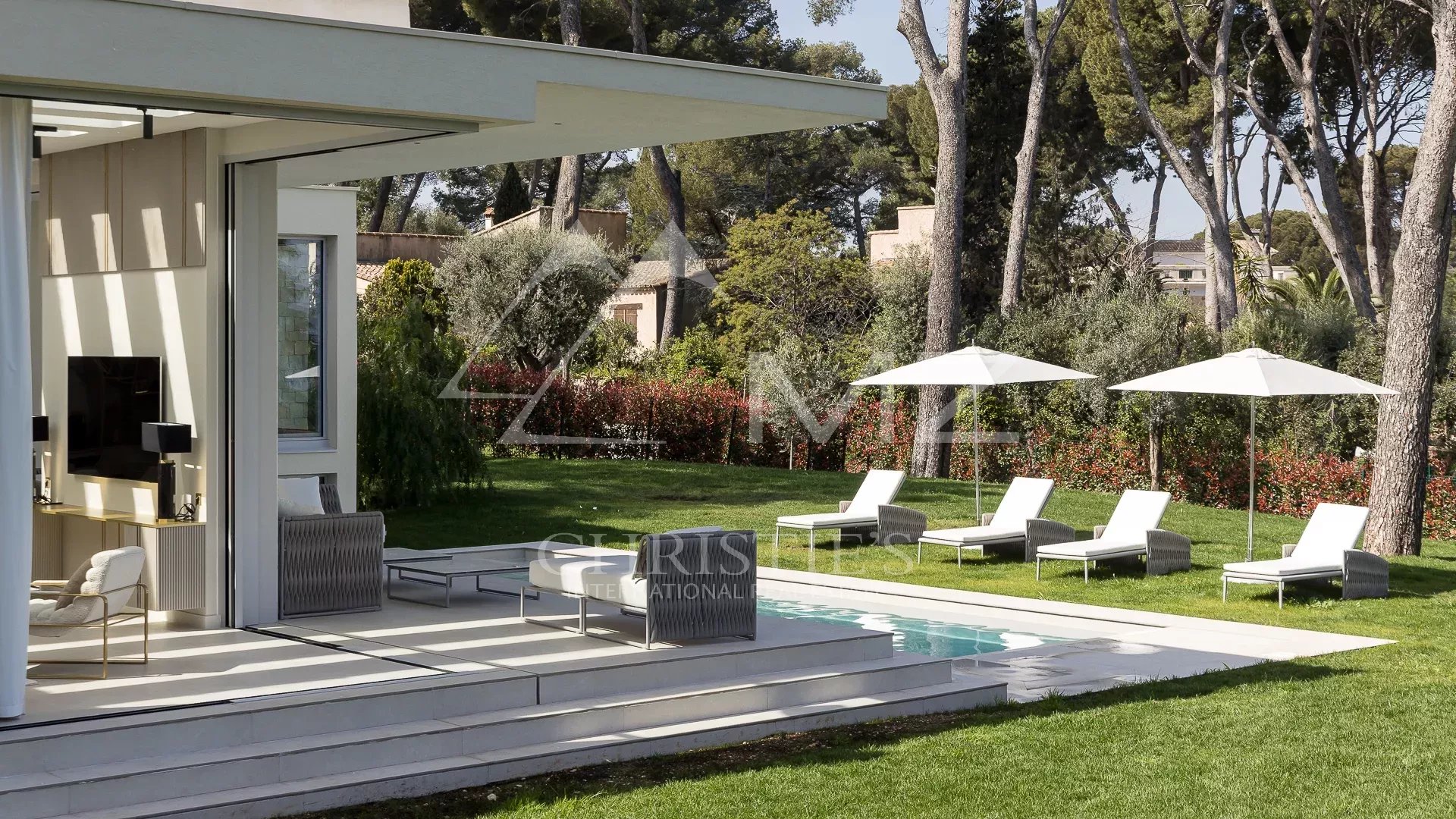 Villa moderne avec piscine et chaises longues dans un jardin verdoyant à Antibes.