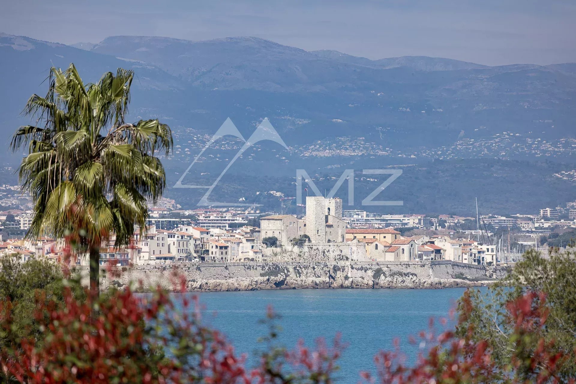 Vue panoramique sur la mer depuis une villa à Cap d'Antibes, avec des montagnes en arrière-plan.