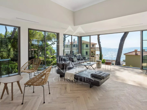 Intérieur d'une villa rénovée avec vue sur la mer, fenêtres panoramiques et mobilier moderne.