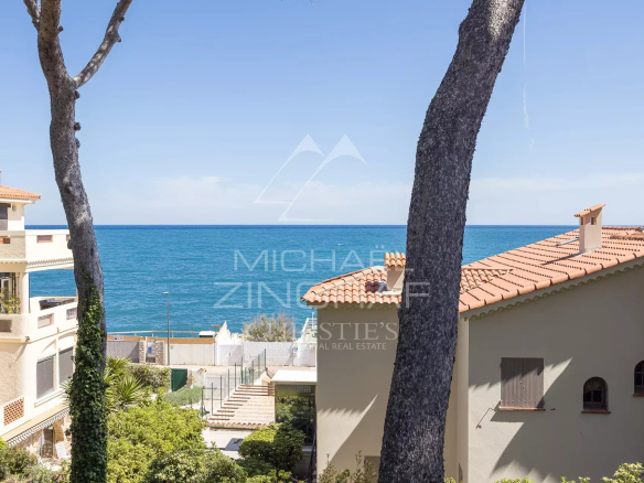 Vue de la mer depuis une villa rénovée à Cap d'Antibes, entourée de végétation et de bâtiments.