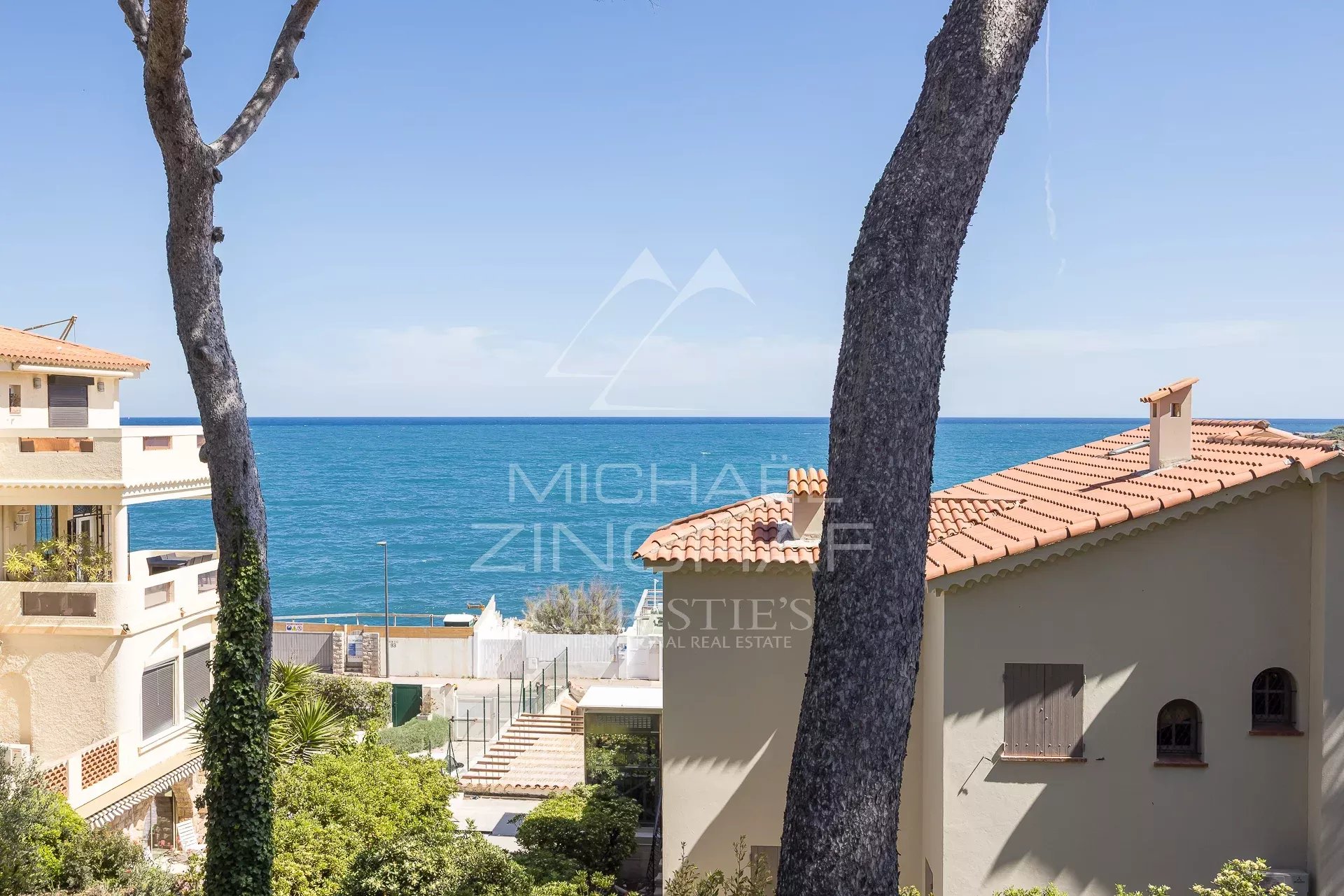 Vue mer depuis une villa à Cap d’Antibes Vue de la mer depuis une villa rénovée à Cap d'Antibes, entourée de végétation et de bâtiments.