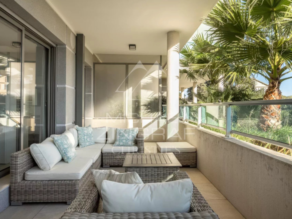 Terrasse d'un appartement moderne au Cap d'Antibes avec mobilier en osier et vue sur des palmiers.