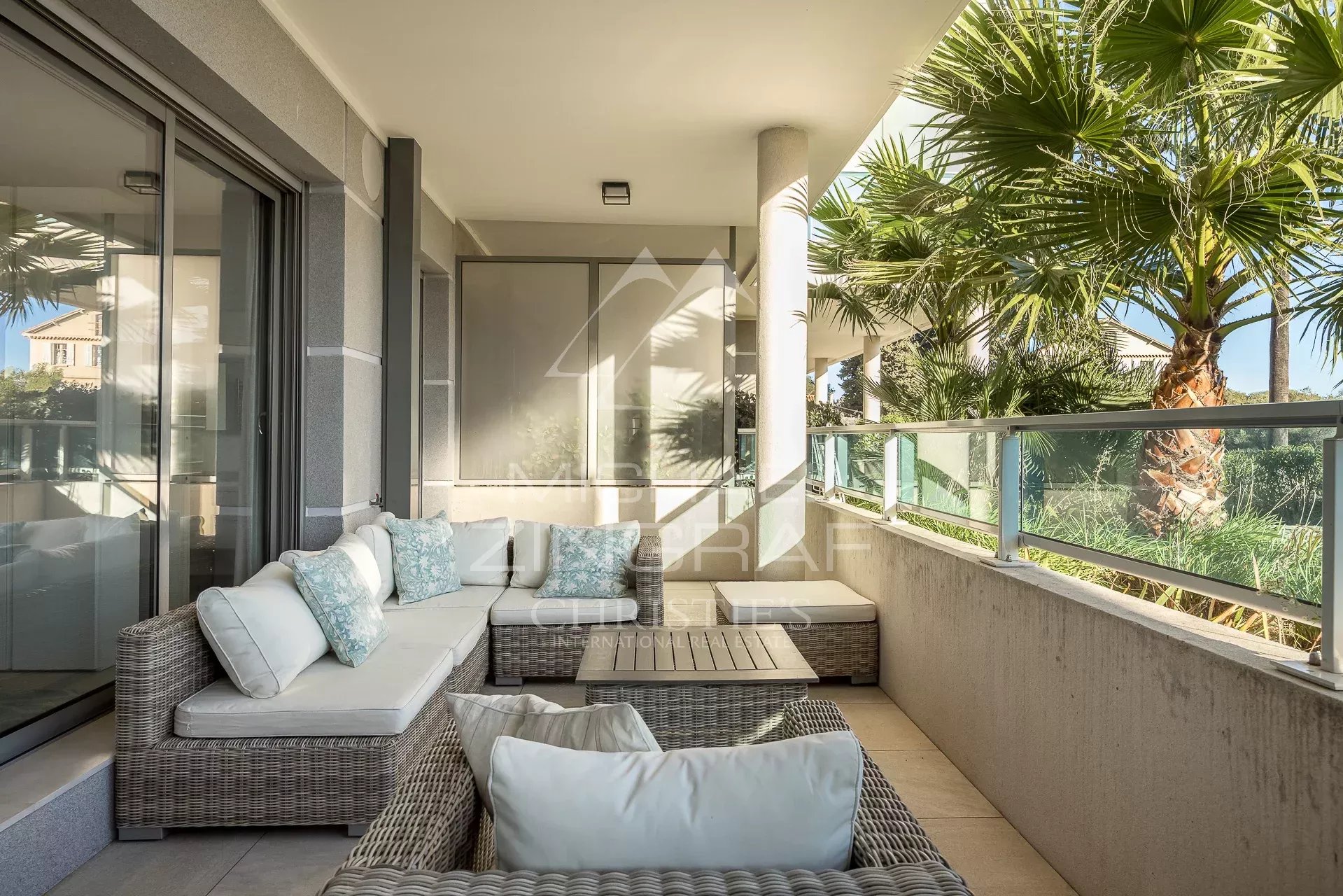Terrasse d’appartement au Cap d’Antibes Terrasse d'un appartement moderne au Cap d'Antibes avec mobilier en osier et vue sur des palmiers.